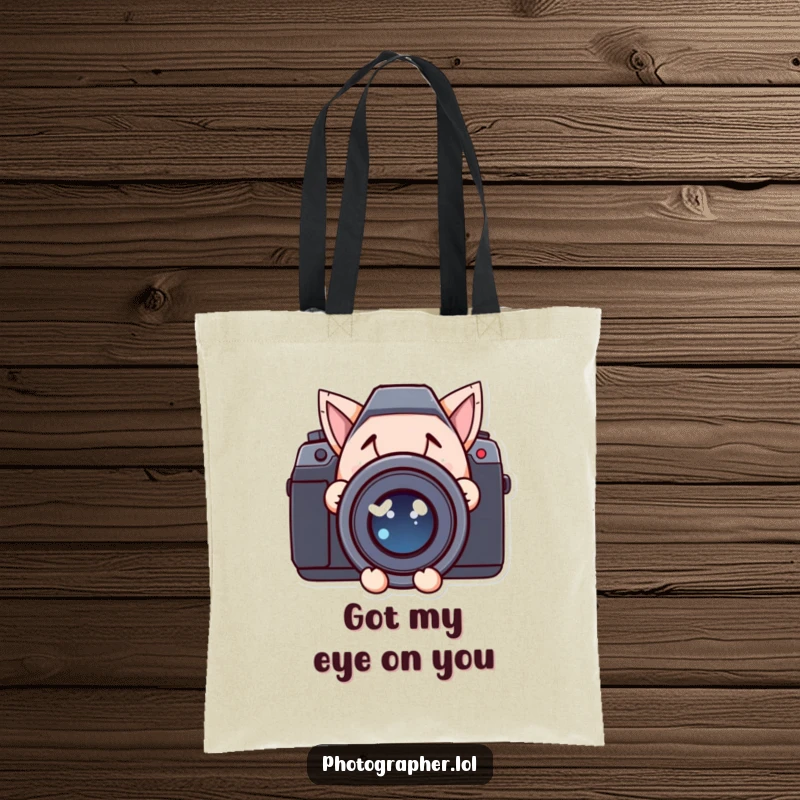Funny tote bag showing a character with a mischievous smile peeking from behind a large camera lens, great for carrying items.